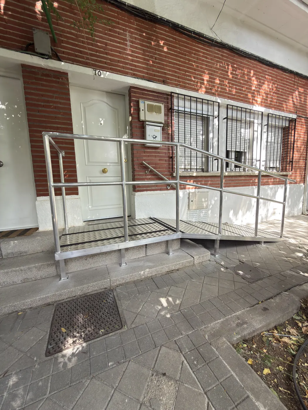 Rampa de acceso metálica con barandilla y peldaño de chapa lagrimada instalada en un portal de Madrid
